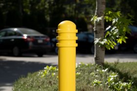 A bright yellow bollard is highly visible in a parking lot full of cars
