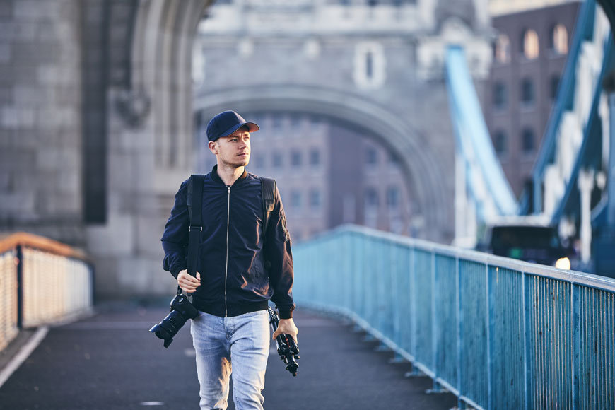 A young male photographer walks over the Tower Bridge in London