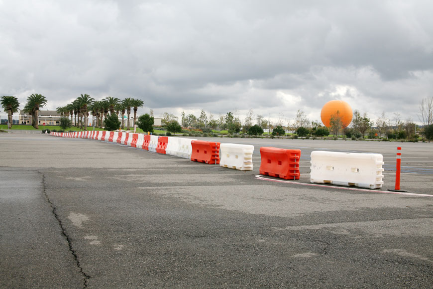 Orange and white plastic barriers divide a parking lot surrounded by palm trees