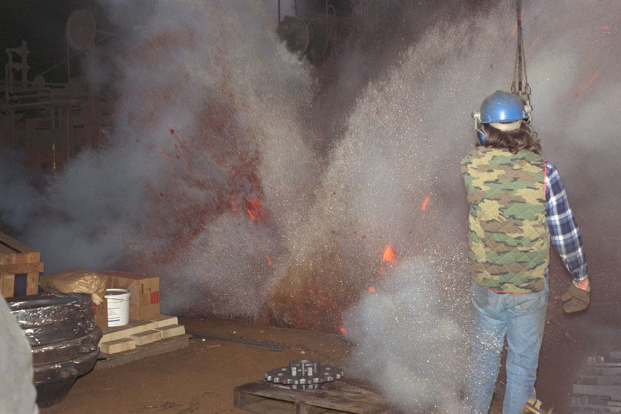 A foundry worker is surrounded by a fiery nimbus of sand during a quenching explosion