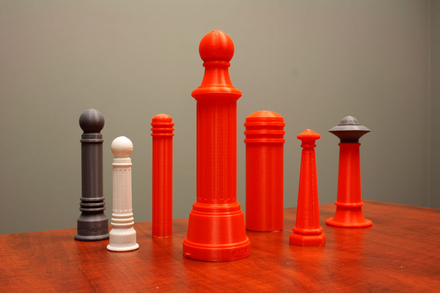A series of small plastic model bollards in orange, white, or grey stand on a table