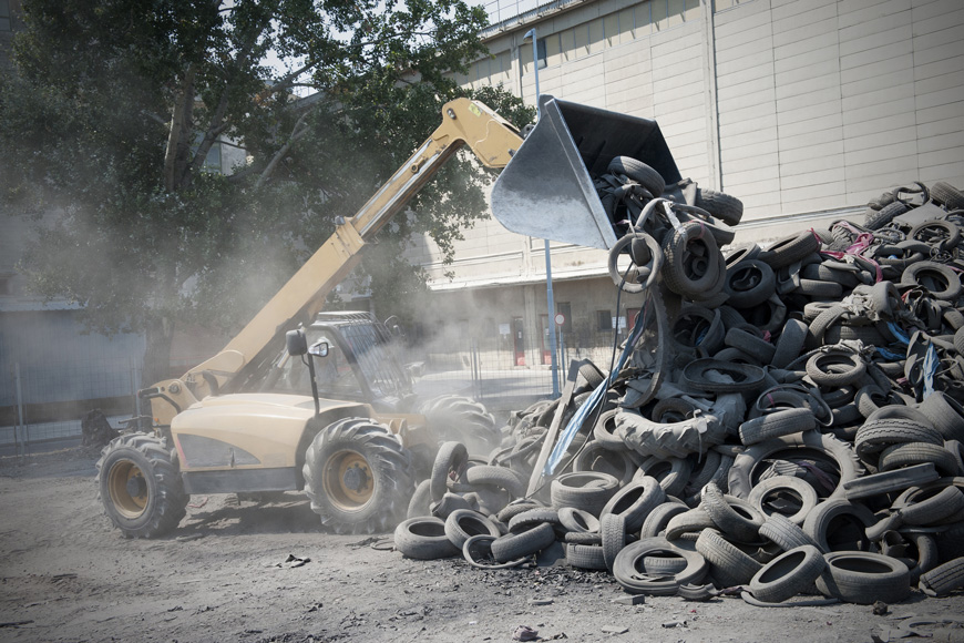 Tires are transported by an excavator for shredding at a tire recycling facility