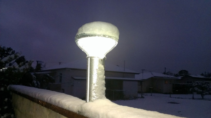 A solar bollard shines beneath a thick cover of snow