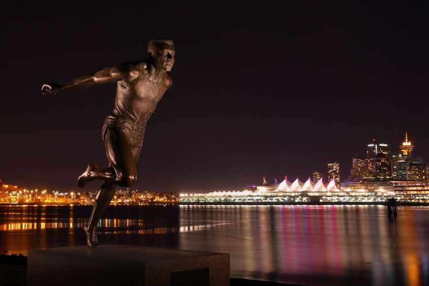 A casting of a runner stands on a pedestal on the Vancouver seawall at night