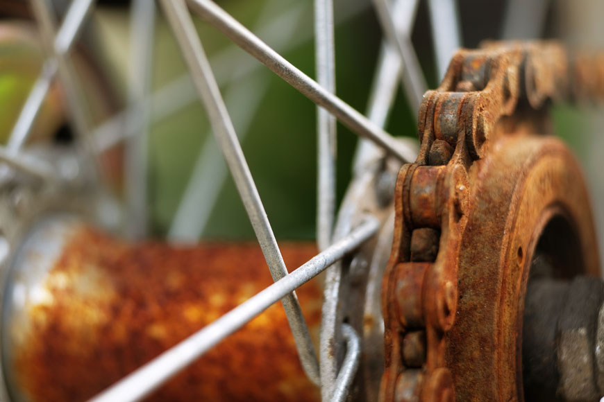 A close-up photo shows a bike chain covered in rust around a wheel dotted with small rust patches
