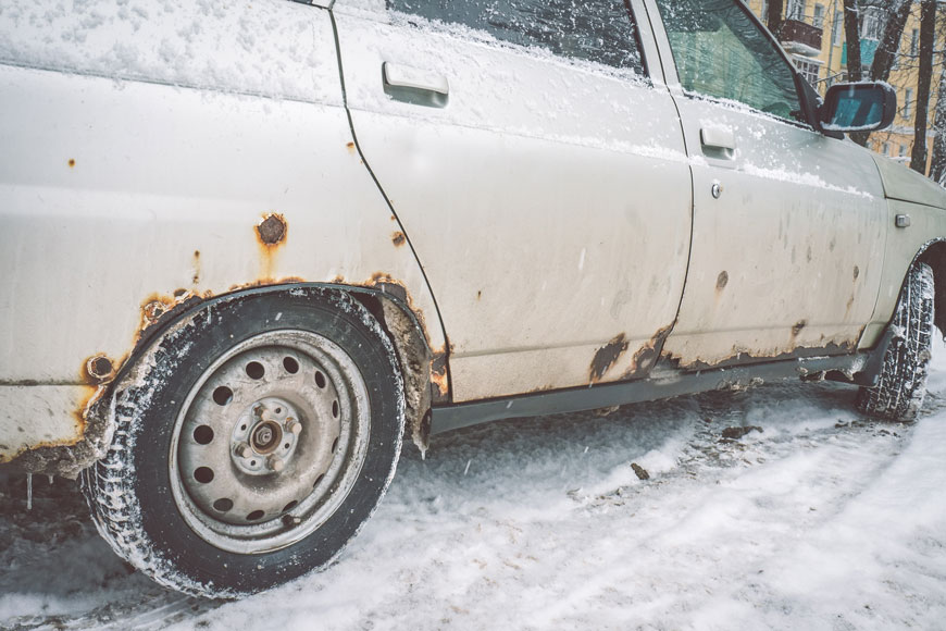 The rusted side of a car in the snow shows the effects of de-icing materials on steel
