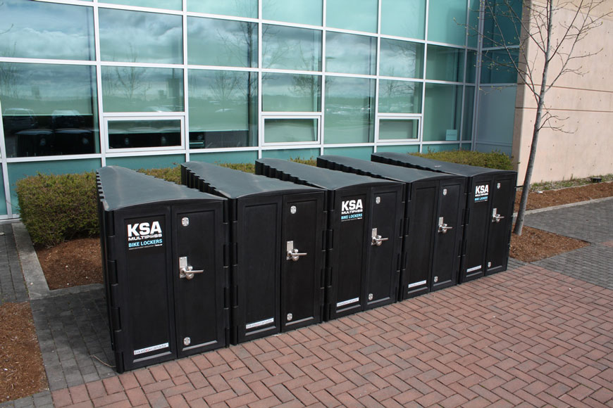 Several black bike lockers stand outside an office tower