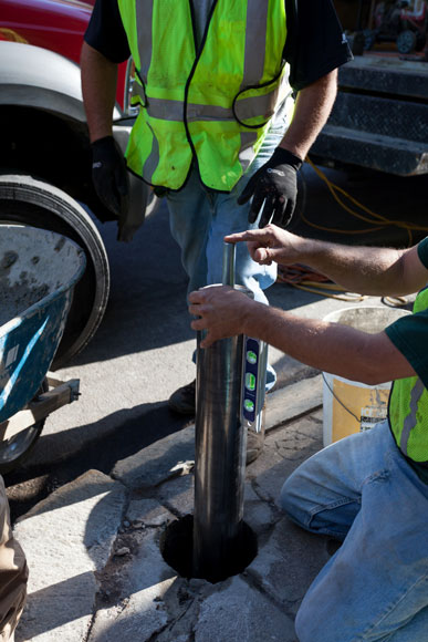 Workers set the interior steel pipe bollards in their installation holes, outside Fenway Park.