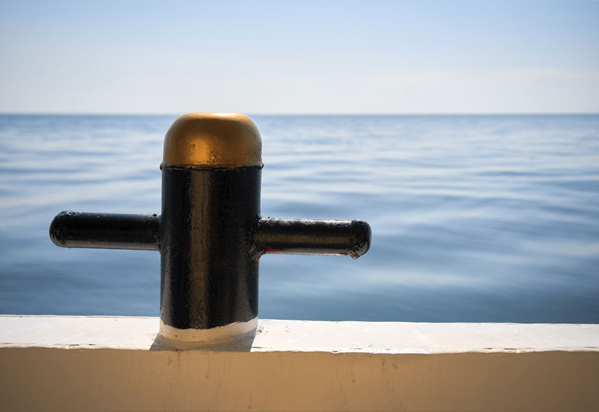 A black post with a gold top has two pegs on either side: sea in background.