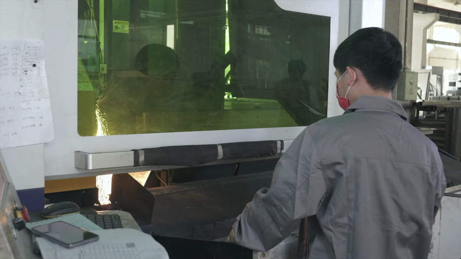 A factory worker stands in front of a CNC laser cutter.