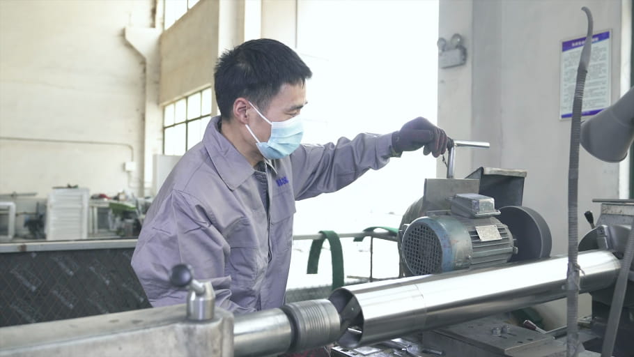 A worker uses a polisher to finish a stainless bollard.