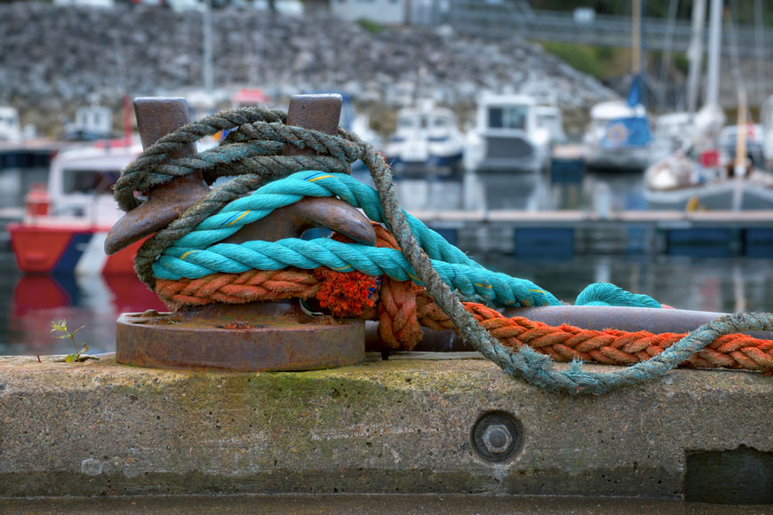 A series of colorful hawsers are draped over a staghorn bollard on a Scottish marina