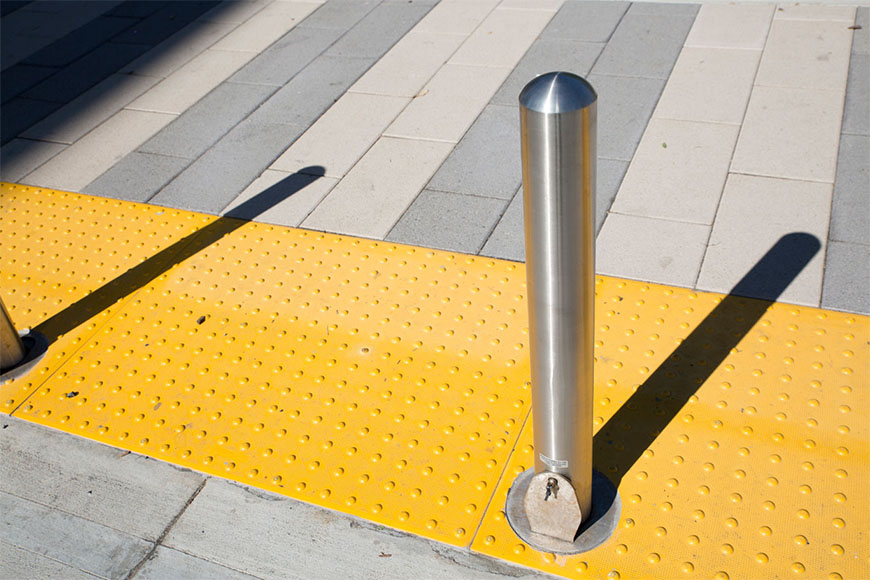 Stainless steel bollards mounted on detectable warning plates along a walkway