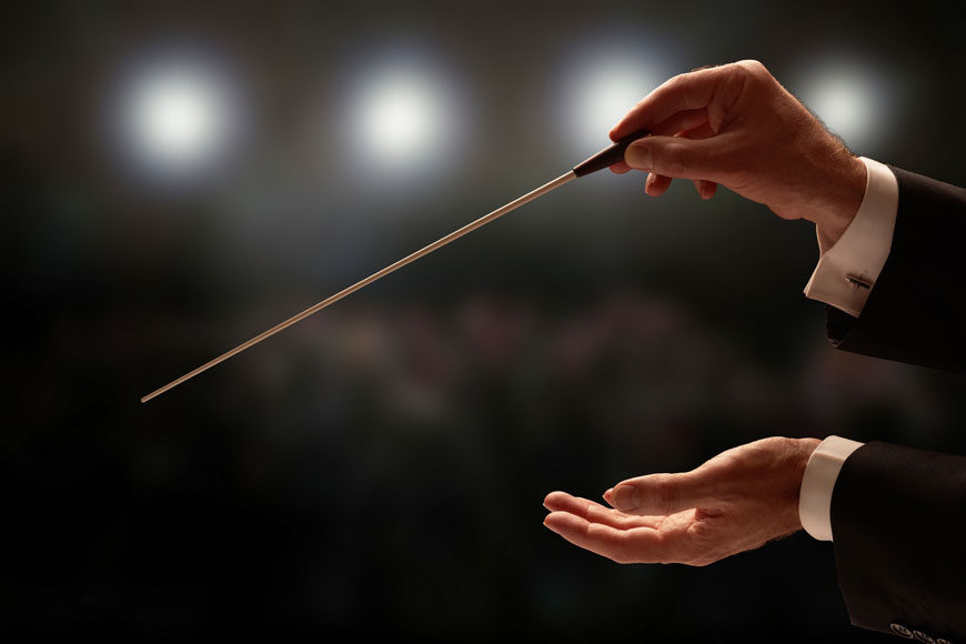 A conductor holds their baton with an audience in the background