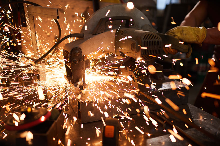 A metal worker grinds an object, throwing a shower of sparks