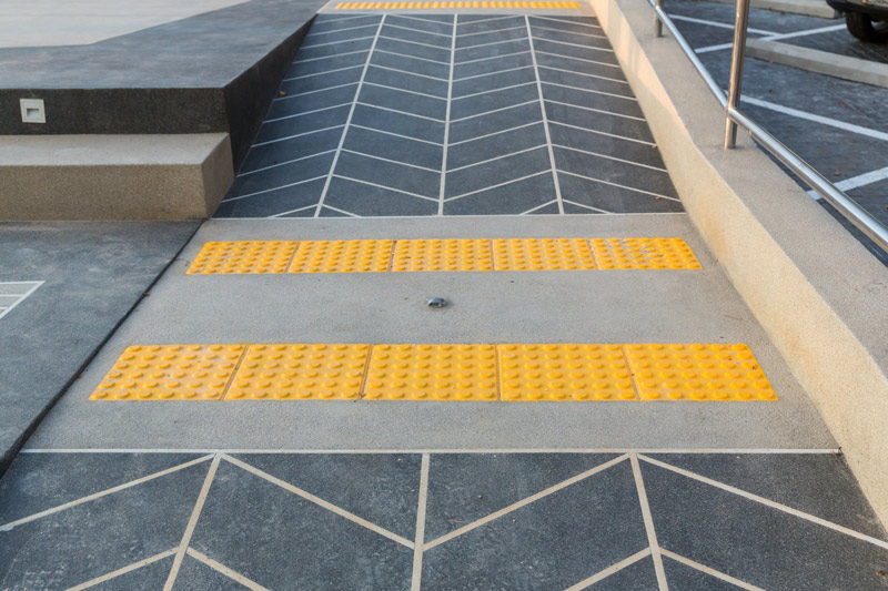 Two strips of tactile paving at the bottom of a two- directional ramp warn of changes in both directions.