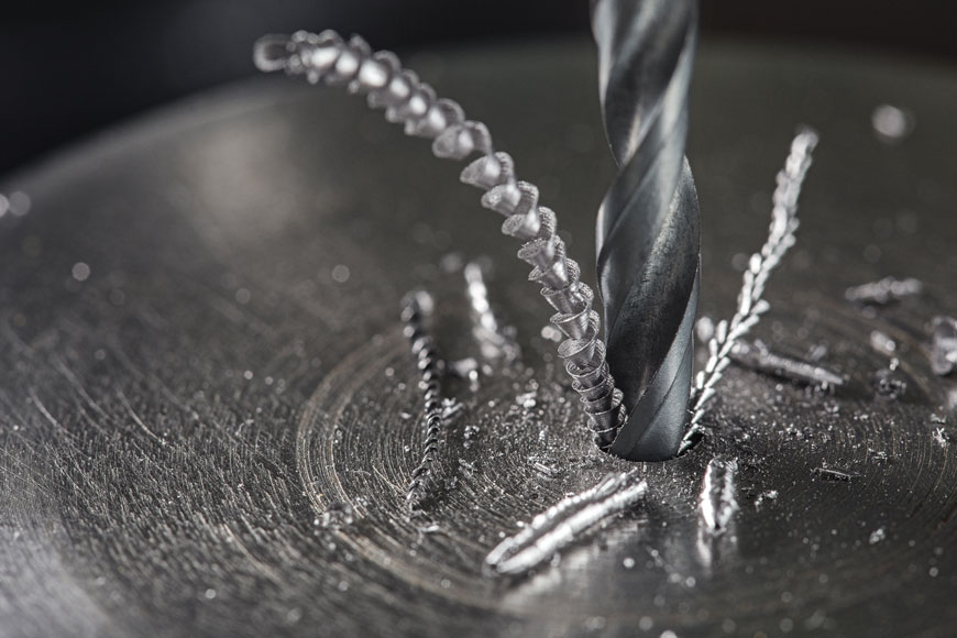 A drill bit bites into a piece of metal and a curl of metal is pulled away