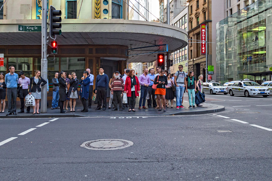 A cluster of people wait for the light to change at an intersection in an urban streetscape
