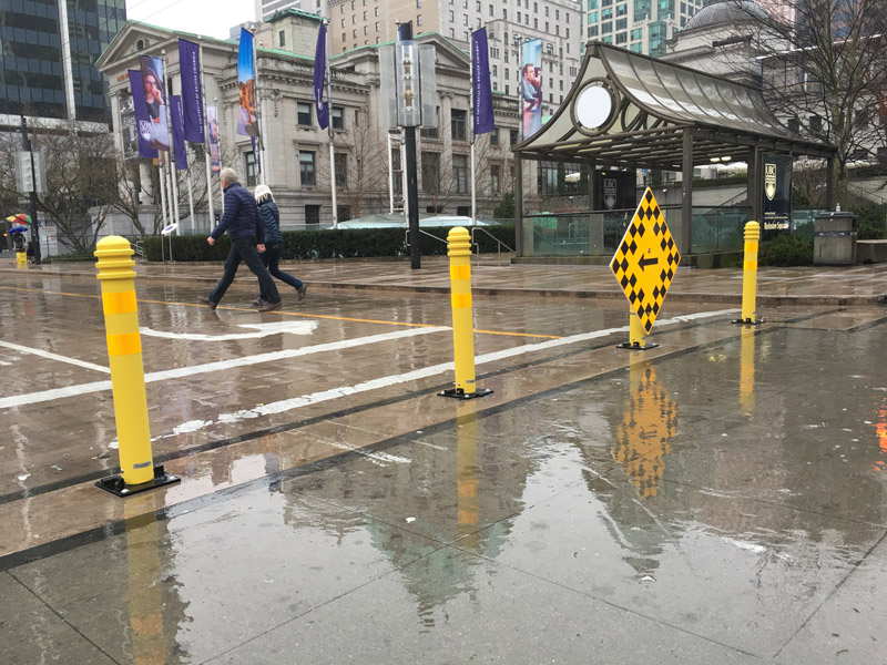 Yellow bollards made of steel and capped with annular rings close a section of Robson St. in Vancouver