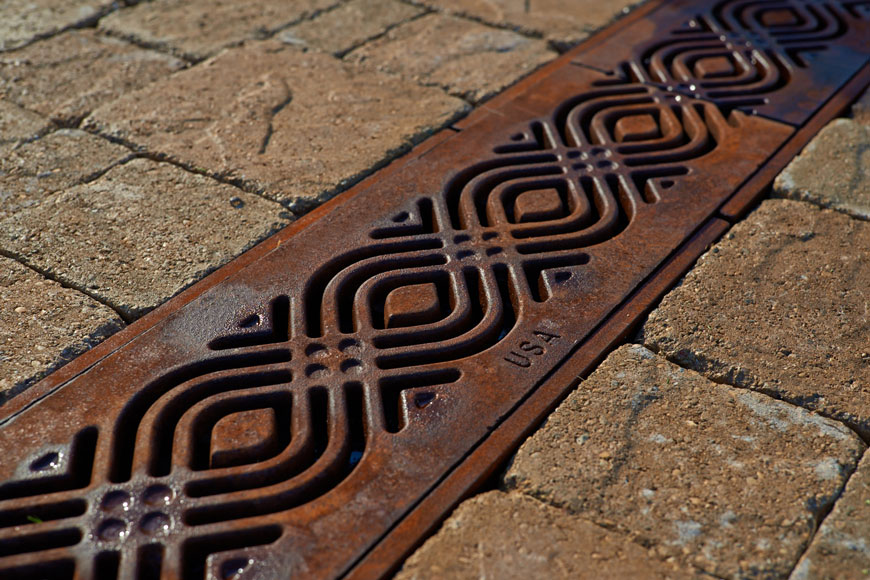 Water soaks into a decorative cast iron grate red and brown with developing patina