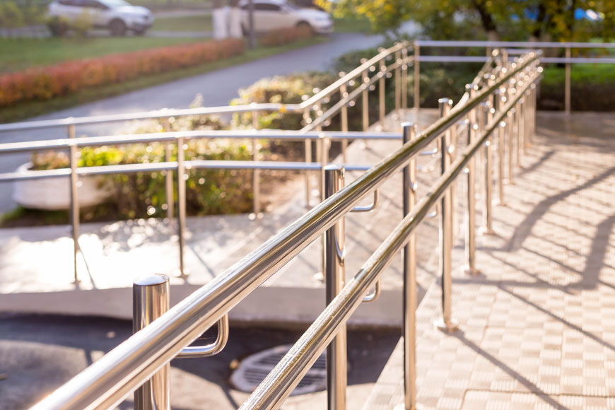 A gleaming stainless steel handrail lines a ramp to a building