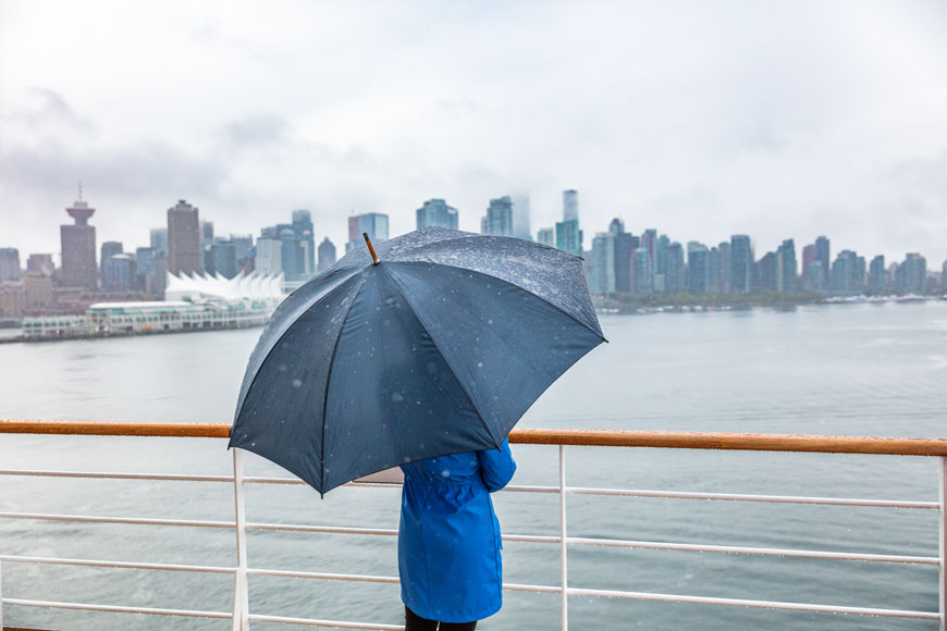 A woman stands under an umbrella near the port of Vancouver watching cruise ships come in