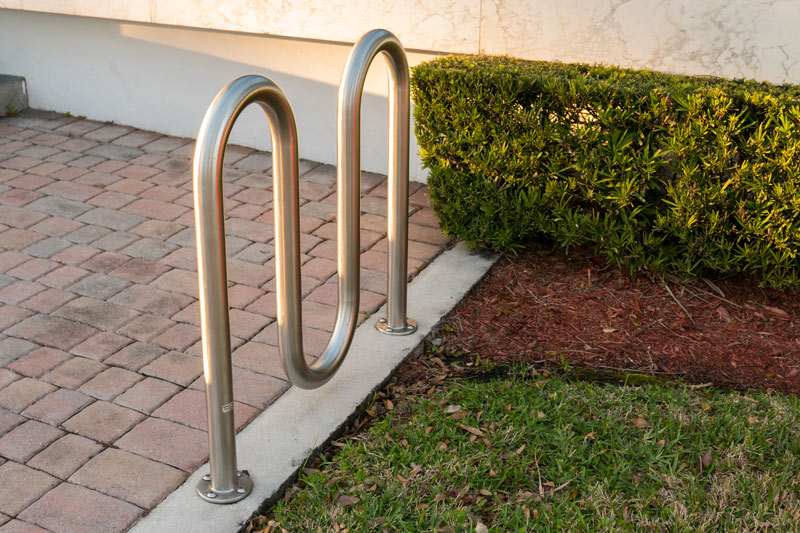 A 3-wave bike rack is placed between grass and stone walkway.