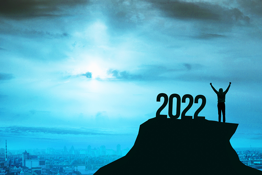 A man stands with hands held high on a hilltop in front of a sunrise with the numbers 2022 beside him