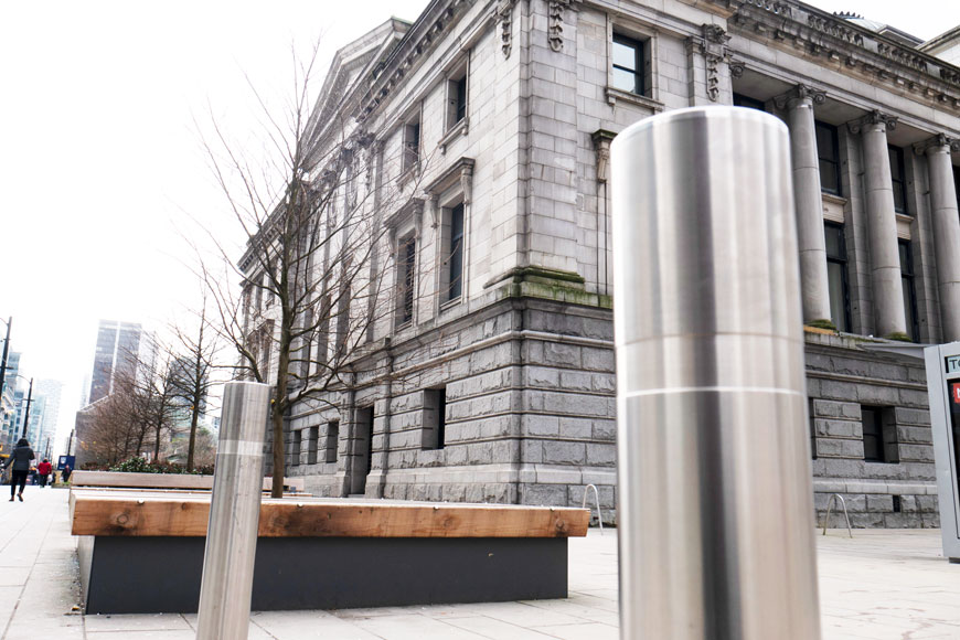A gleaming stainless steel bollard sits in front of a classical building with columns