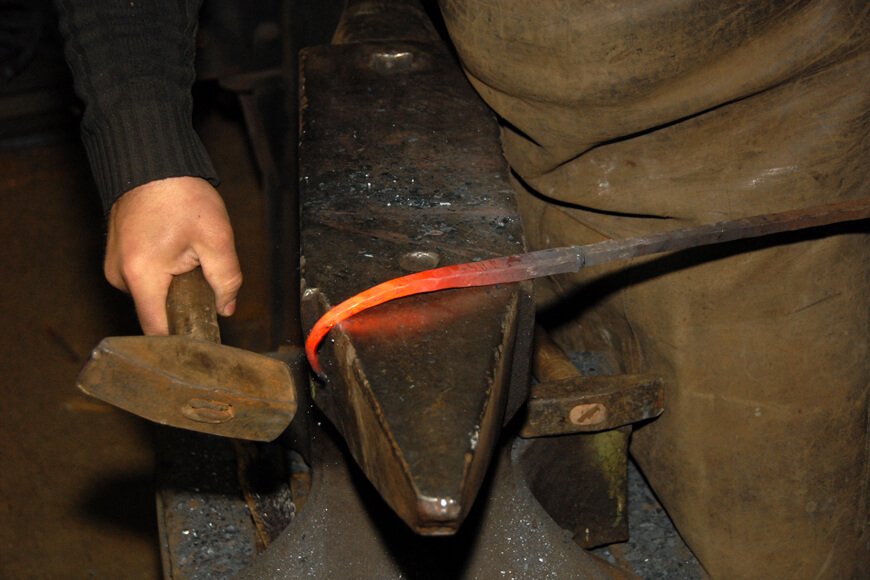 A blacksmith works wrought iron in a foundry