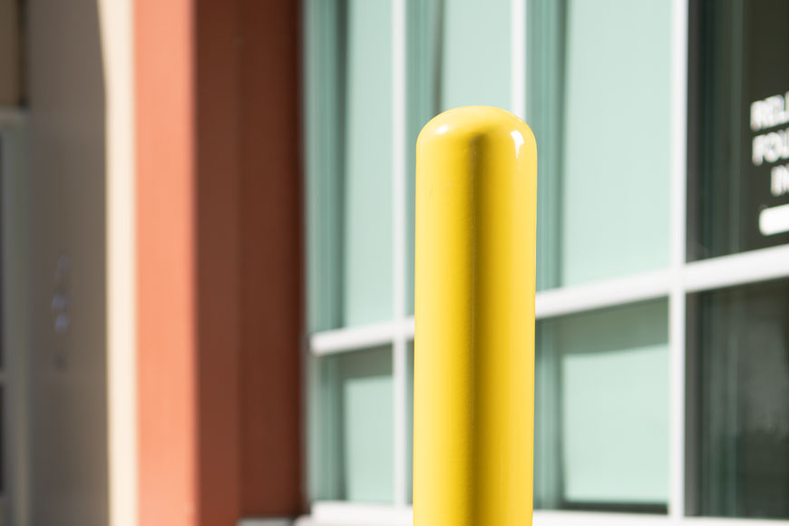 A yellow safety bollard stands protects the glass windows of a business