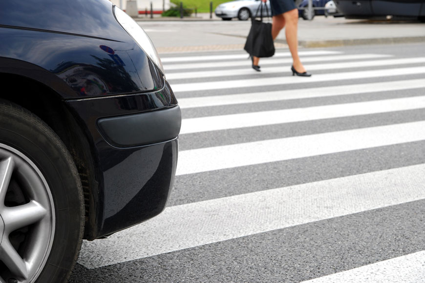 A business woman wearing heels walks through a zebra crossing while a car waits